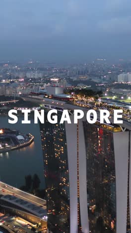 Vertikale-Video-Drohnenaufnahme-Der-Skyline-Und-Des-Hafenviertels-In-Der-Abenddämmerung,-überlagert-Mit-Einer-Animierten-Grafik,-Die-Singapur-Darstellt