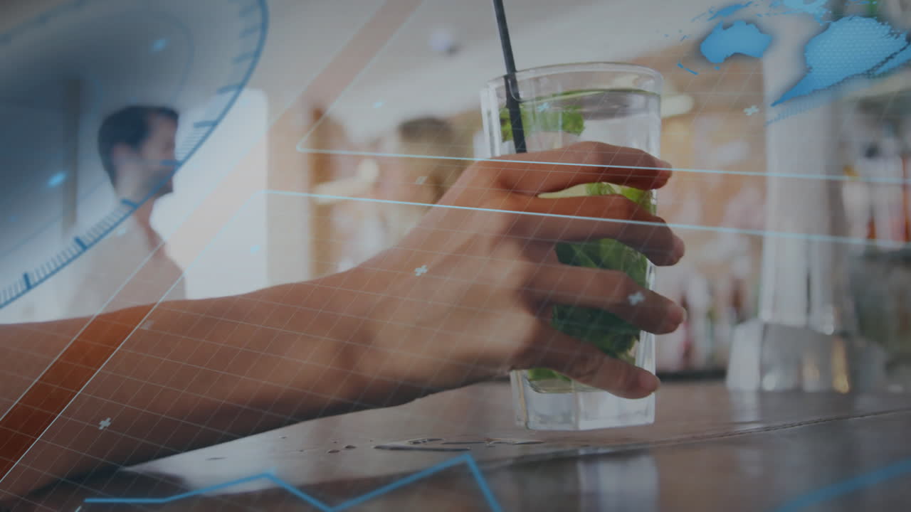 Hand grasping glass of mint drink at bar counter, showing floating data, map outlines in technology