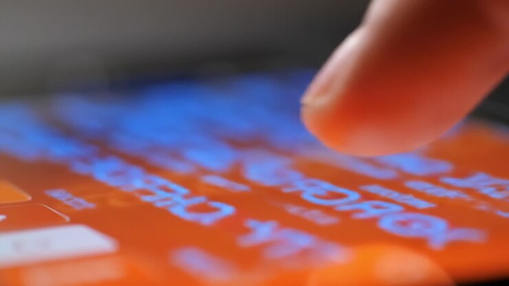 Close-Up Focus on a Finger Tapping an Interactive Screen Display with Vibrant Orange Background and Text in Bright Blue, Indicating Engaging Digital Interaction