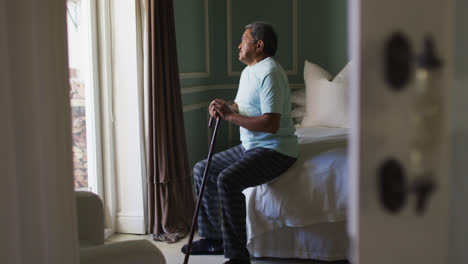 senior mixed race man with walking stick sitting down on bed