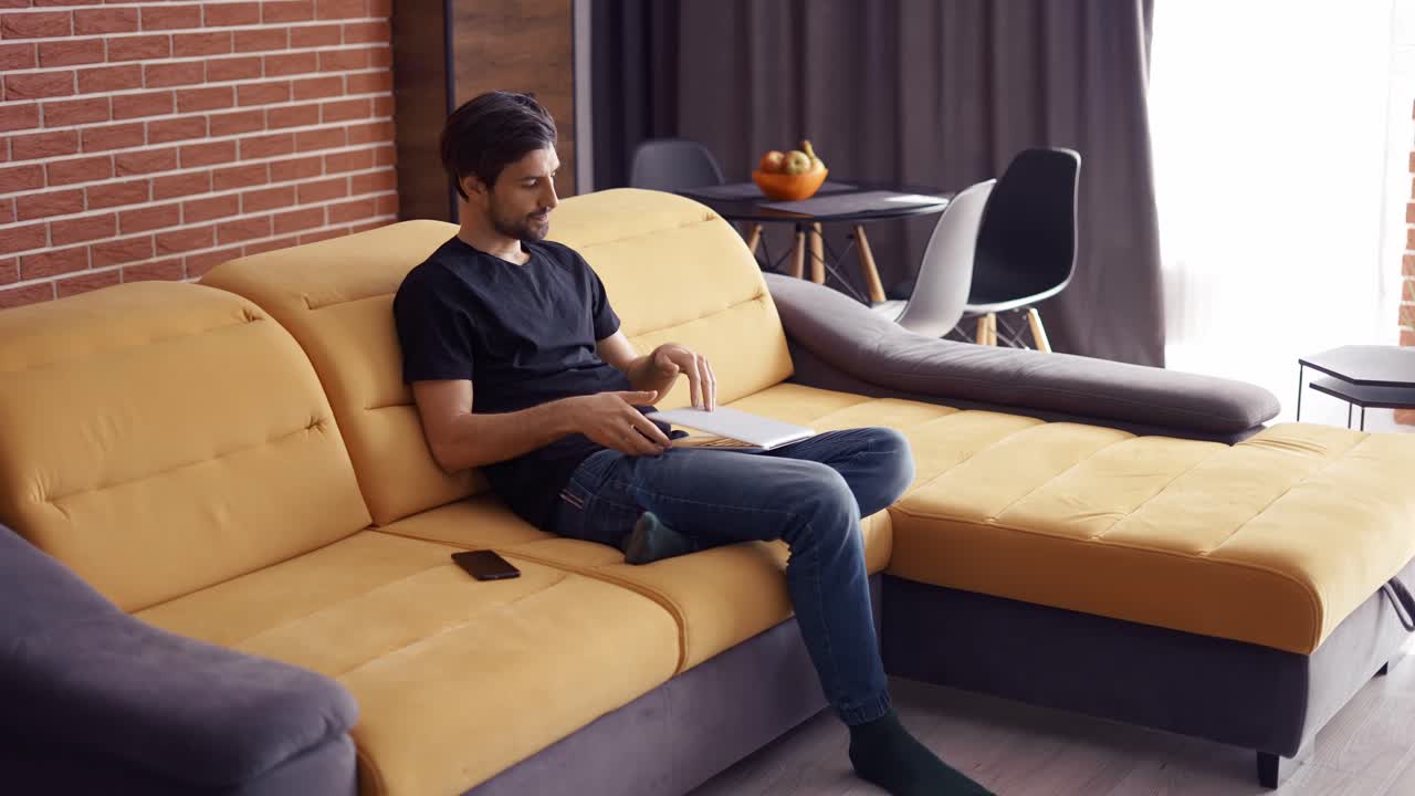 어두운 머리카락의 남자가 집에서 노트북에서 일합니다.