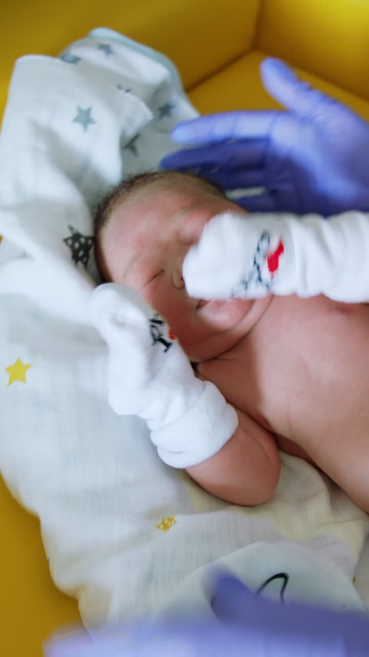 Little baby lying on the yellow table is taken care by a nurse. Medic undresses the newborn child. Vertical video