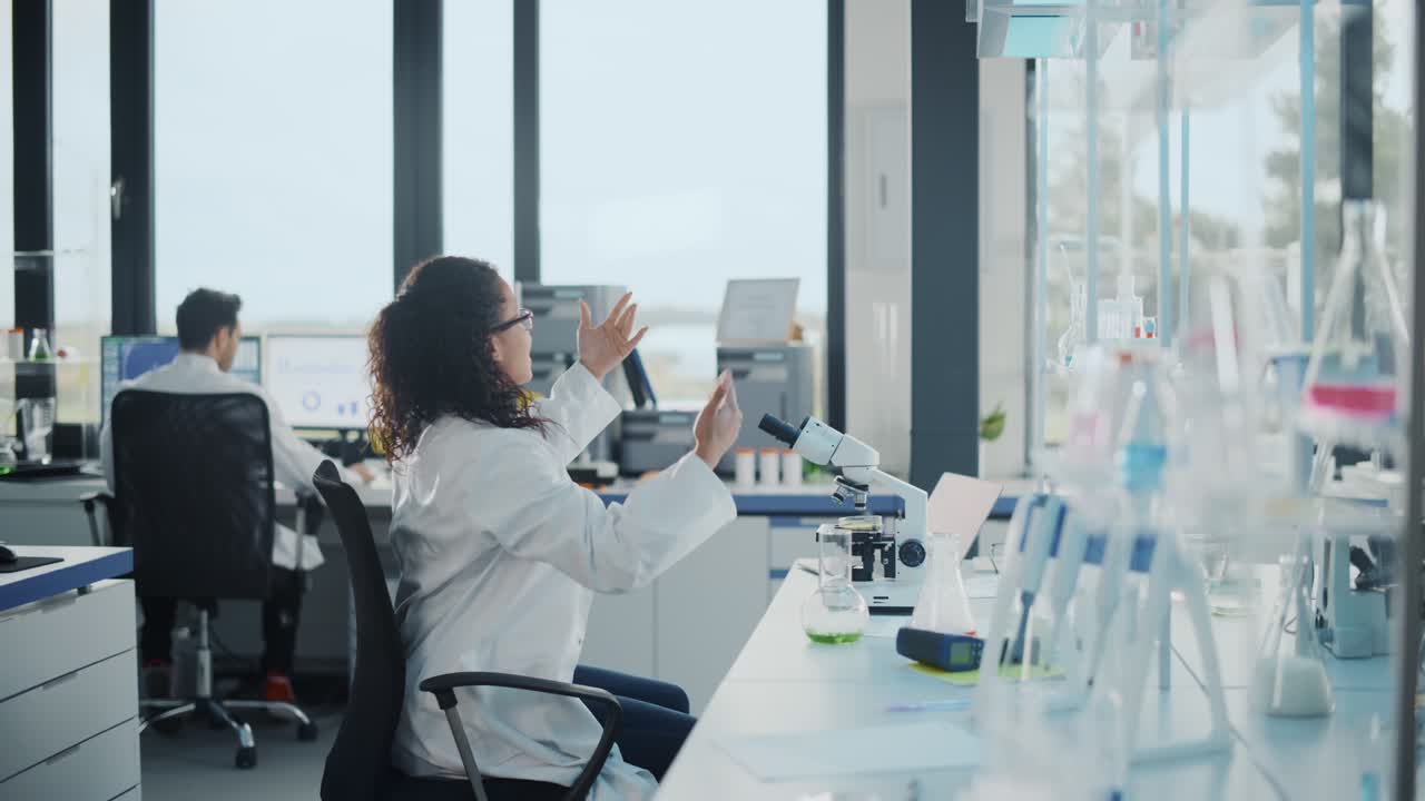 laboratorio de ciencias médicas: hermosa científica negra mirando bajo el microscopio, descubre un nuevo compuesto farmacéutico, llama a sus colegas a celebrar. jóvenes especialistas felices, haciendo experimentos innovadores