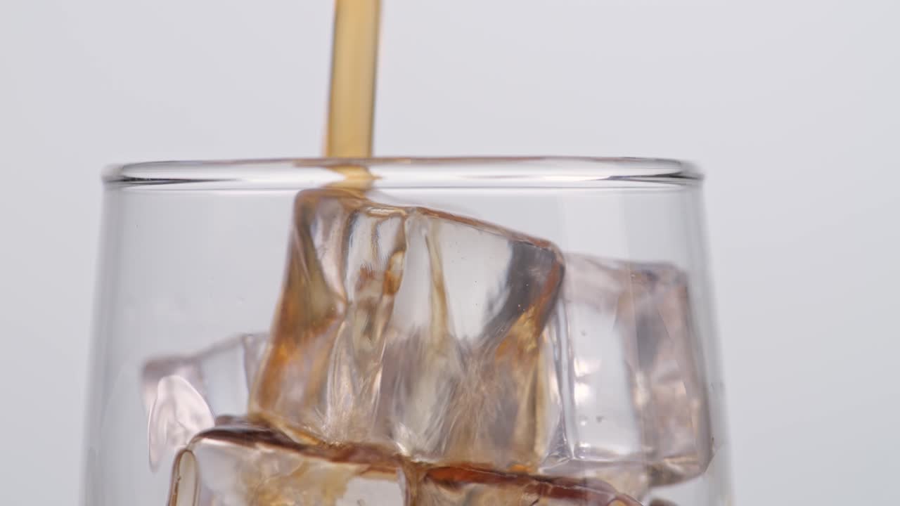 Primo piano di cola fresca versata nel bicchiere con cubetti di ghiaccio su sfondo bianco