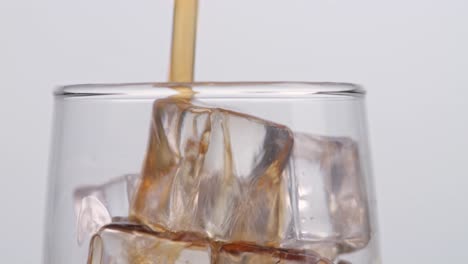 cerca de cola fresca que se vierte en el vaso con cubos de hielo en fondo blanco