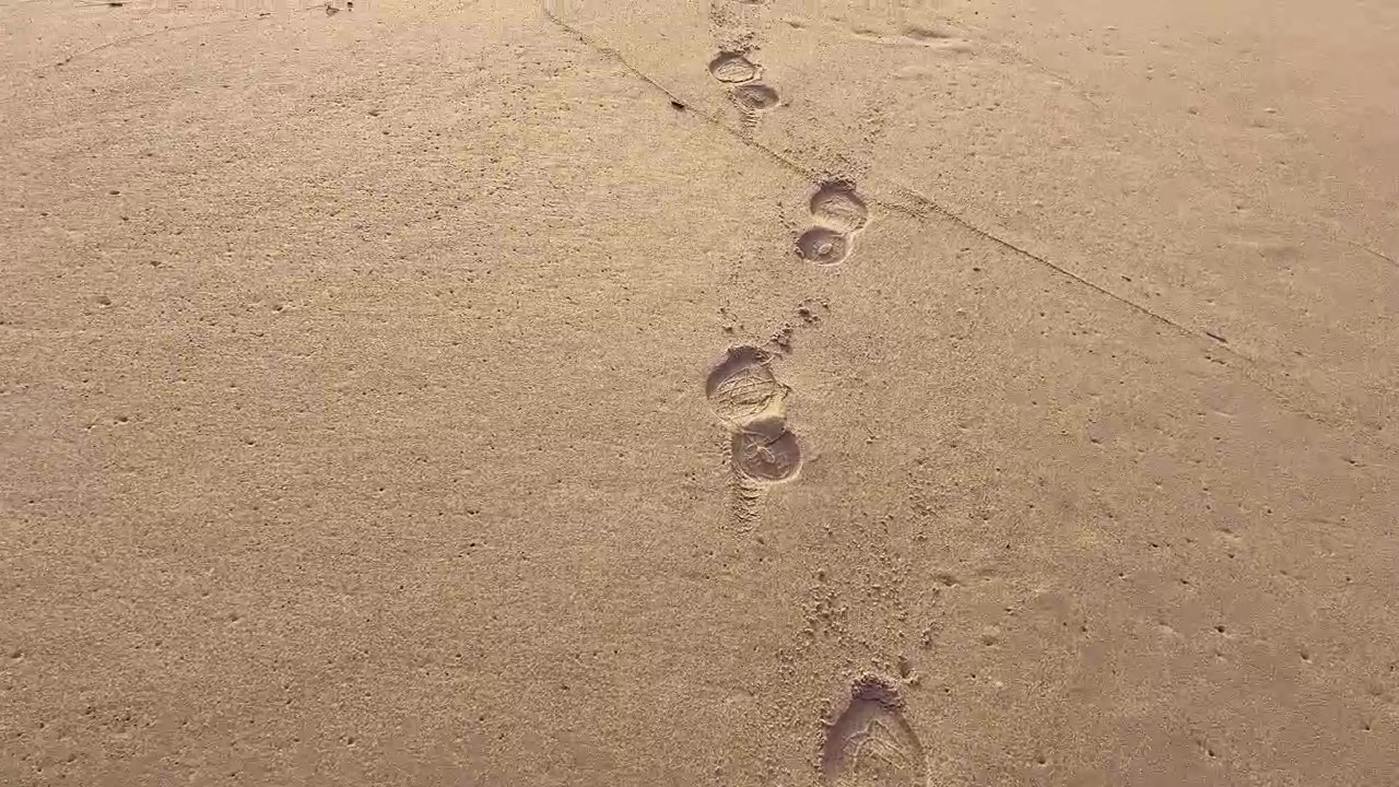 Pegadas criando um caminho na areia lisa da praia de Barbate, na Andaluzia, Espanha, oferecendo uma vista serena de uma caminhada tranquila pela costa.