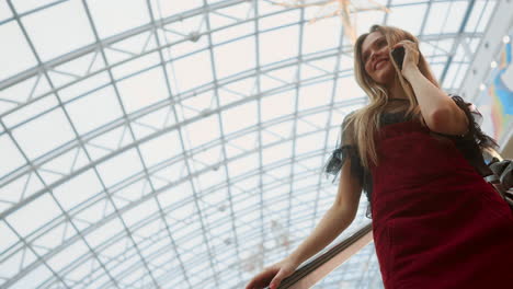 a beautiful girl descends the escalator and talks on the phone in the mall.