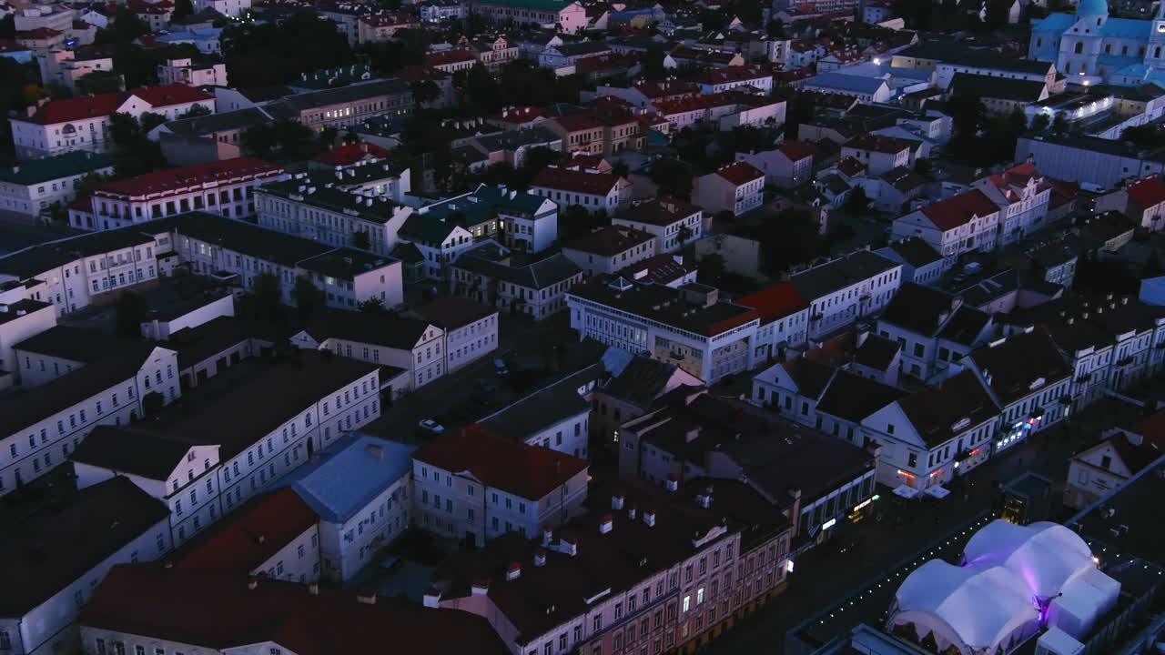 Ripresa aerea cinematografica da drone sulla città di Grodno al crepuscolo, con architettura storica, tetti e cupole di chiese sotto un cielo serale blu in Bielorussia.
