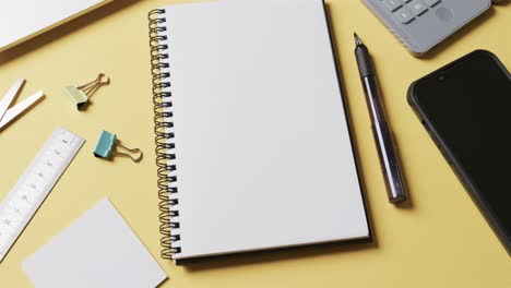 flat lay of pen, notebook and school materials with copy space on yellow background