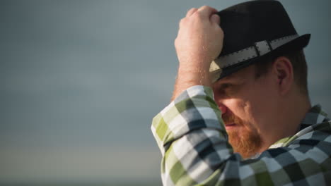 una toma de primer plano de la cara de un hombre, con un sombrero negro con una expresión contemplativa, ambientada contra un telón de fondo de un cielo nublado. la escena captura un momento pensativo