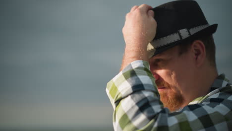 a close-up shot of a man's face, wearing a black hat with a contemplative expression, set against a backdrop of a cloudy sky. the scene captures a thoughtful moment