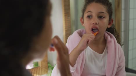 feliz chica de raza mixta cepillándose los dientes en el baño