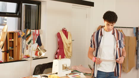 Focused-biracial-male-fashion-designer-sketching-design-standing-at-desk-in-studio,-slow-motion