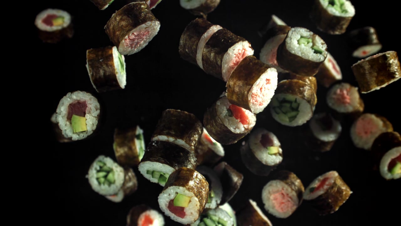 Deliziosi rotoli di sushi che cadono al rallentatore su sfondo nero