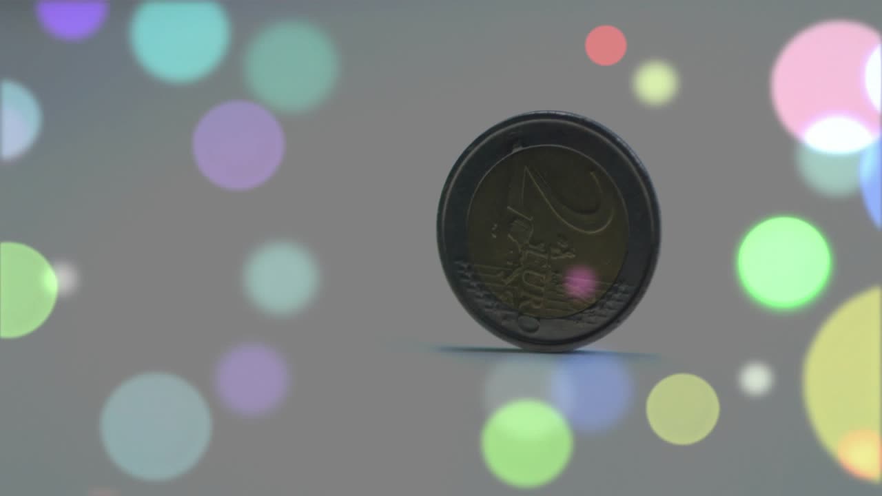 Human finger flicking euro coin flipping onto rim, spinning wobbling on grey surface for physics