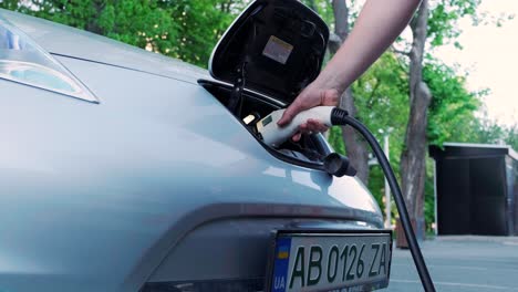 refueling process of an electric car. a shot under the hatch where the electric eco car charges. the electric car charging hatch opens automatically. a male hand inserts an erectile car