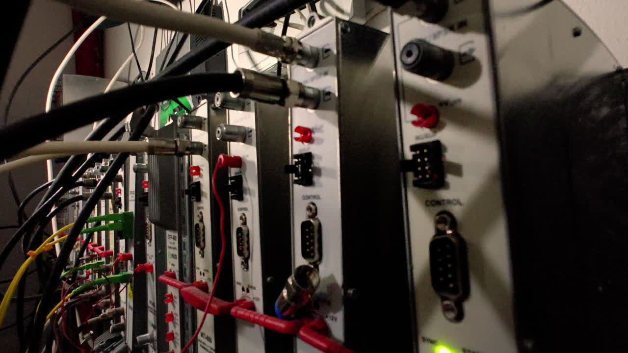 A close-up of a server rack with numerous cables and connectors. The equipment is housed in a dark room, and the lights from the devices create a colorful and intricate pattern.