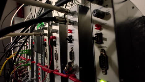 A close-up of a server rack with numerous cables and connectors. The equipment is housed in a dark room, and the lights from the devices create a colorful and intricate pattern.