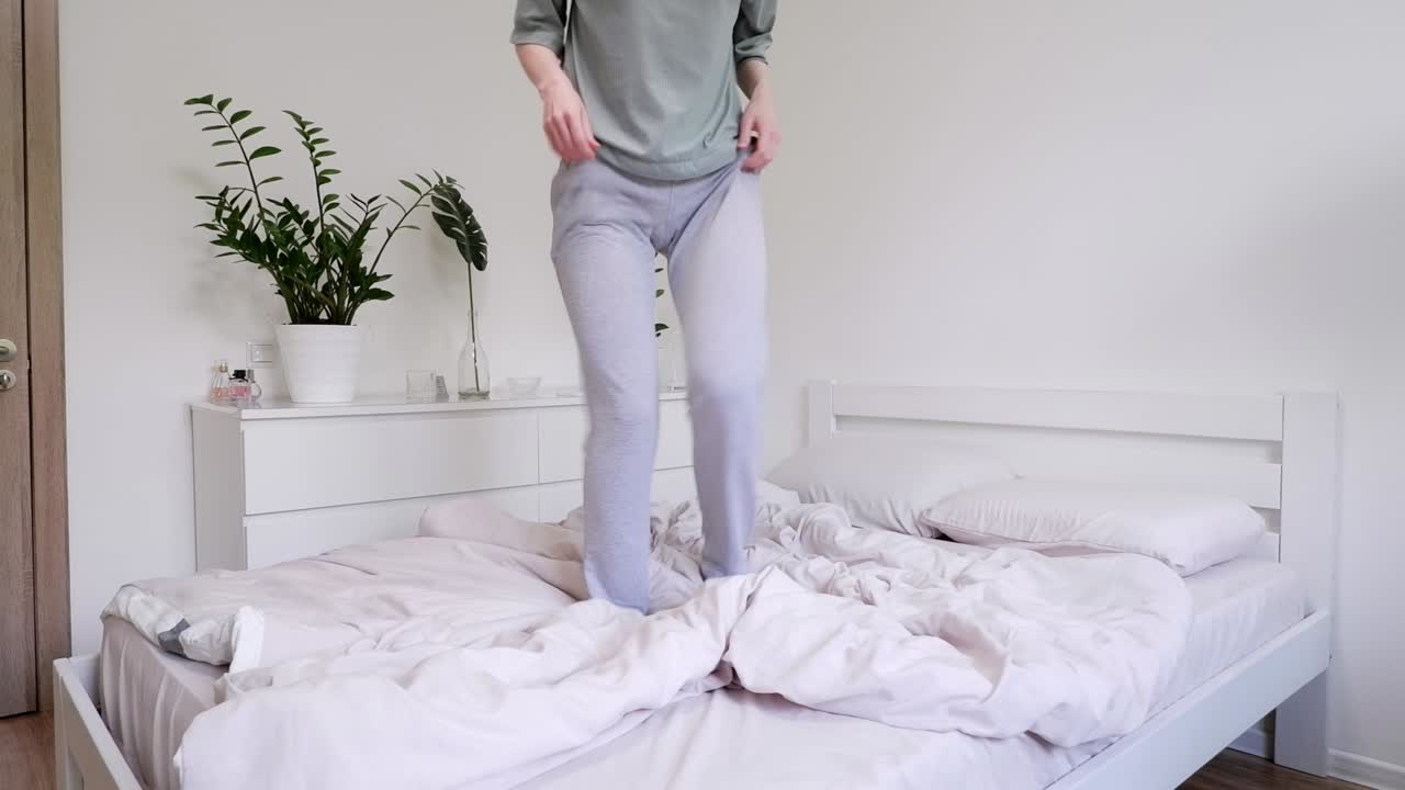 잠옷을 입은 여자가 침대에 뛰어다니고 있습니다. 현대적인 스타일의 아름다운 밝은 방