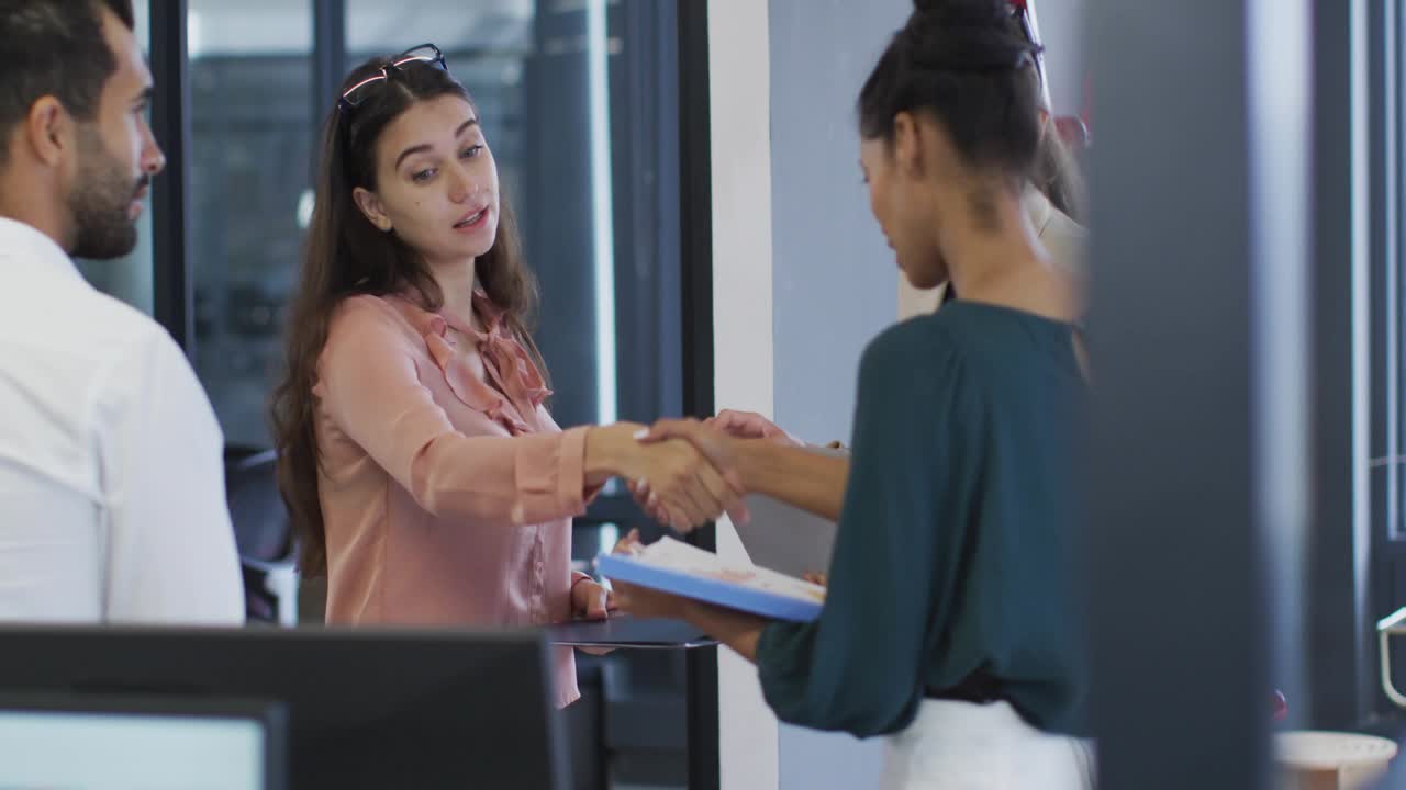 Pink-clad woman with tablet reaching, teal woman holding docs shaking hands, business HUD rising
