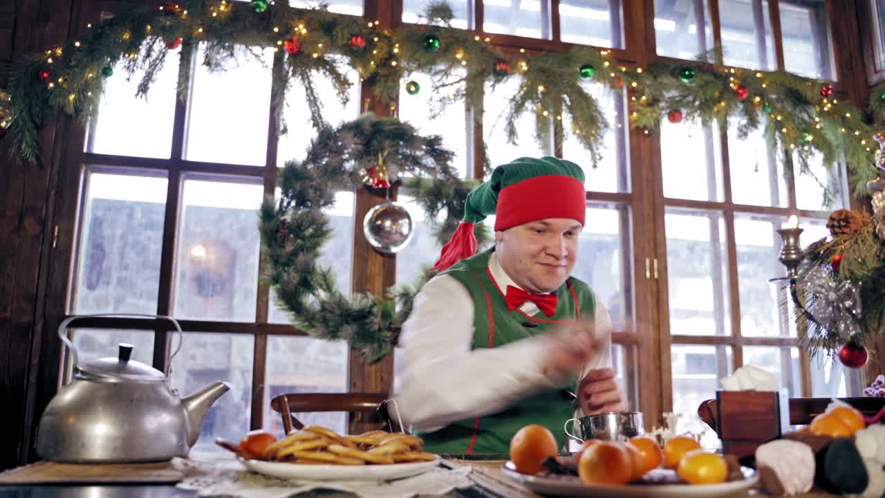 Elf playing tangerines at a table. Santas elf sitting at Christmas table in a decorated room. New Year celebration. Christmas eve.