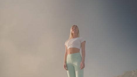 slim athletic woman stands in mist puts hand to head enjoying magical view