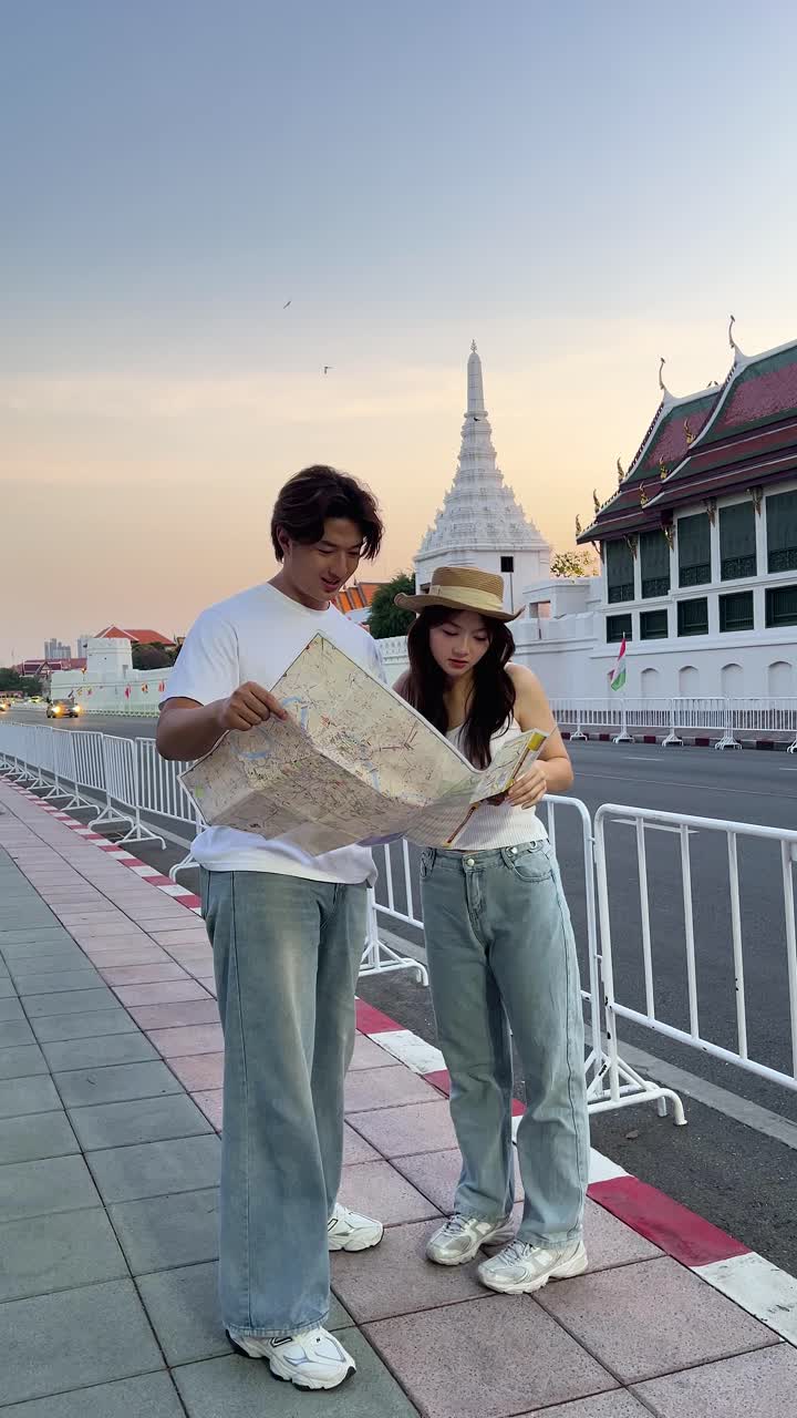 Una coppia consulta una mappa di viaggio accanto a un tempio al tramonto, su una strada urbana, con illuminazione naturale soffusa e inquadratura stabile.