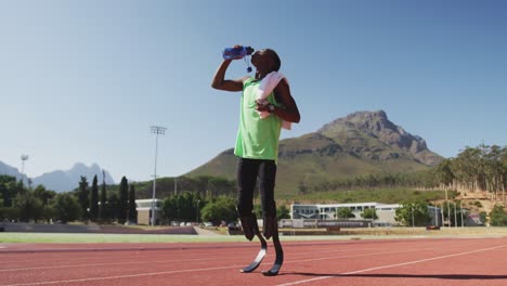 Disabled-mixed-race-man-with-prosthetic-legs-standing-on-a-race-track-and-drinking-water-