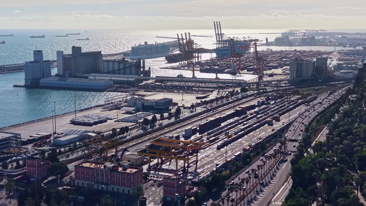 Lungomare industriale del Porto di Barcellona a Barcellona, Catalogna, Spagna, che mostra gru portacontainer, magazzini logistici, binari ferroviari per merci, strade portuali e acqua mediterranea illuminata dal sole, vista aerea.