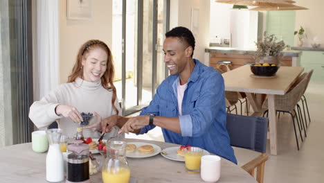 diverse couple enjoying breakfast together, smiling and sharing pancakes at home