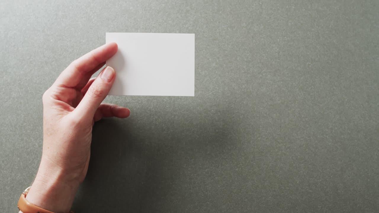 mano de mujer caucásica con tarjeta de visita blanca en fondo gris, espacio de copia, cámara lenta