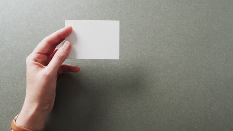 hand of caucasian woman holding white business card on grey background, copy space, slow motion