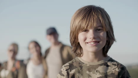 portrait of a little caucasian boy looking at the camera and smiling while his family standing behind in a blurred background