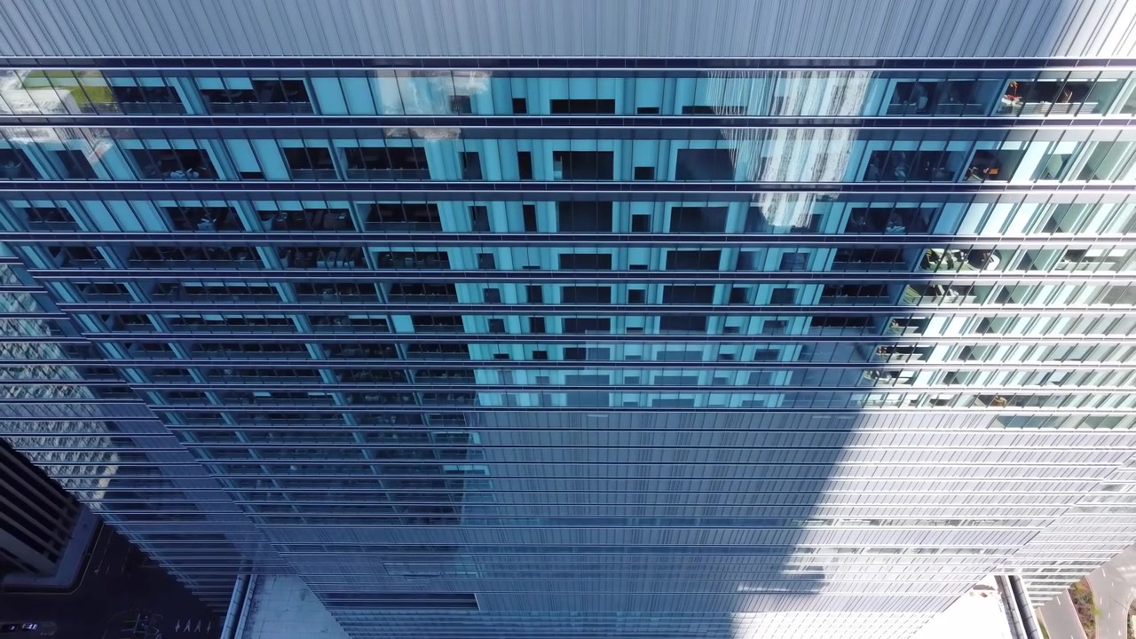 Vista aérea de la fachada de un rascacielos de cristal con ventanas reflectantes, sombra diagonal dramática, equipo en la azotea, calle