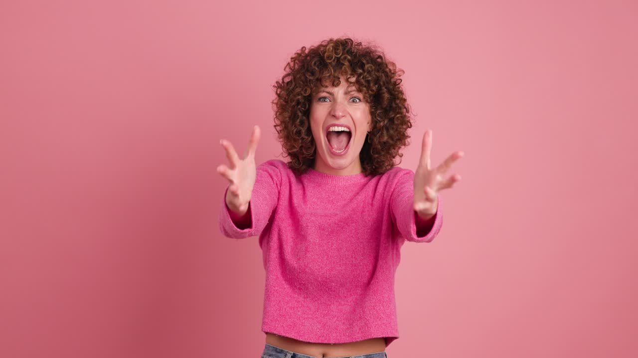 Shocked young woman showing stretched hands with palms on pink background