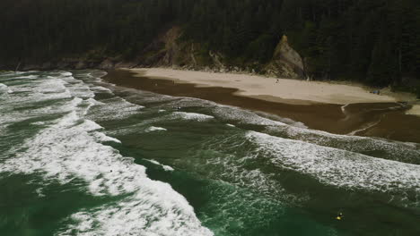 dedicated surfers on remote oregon coast beach, wide aerial push in