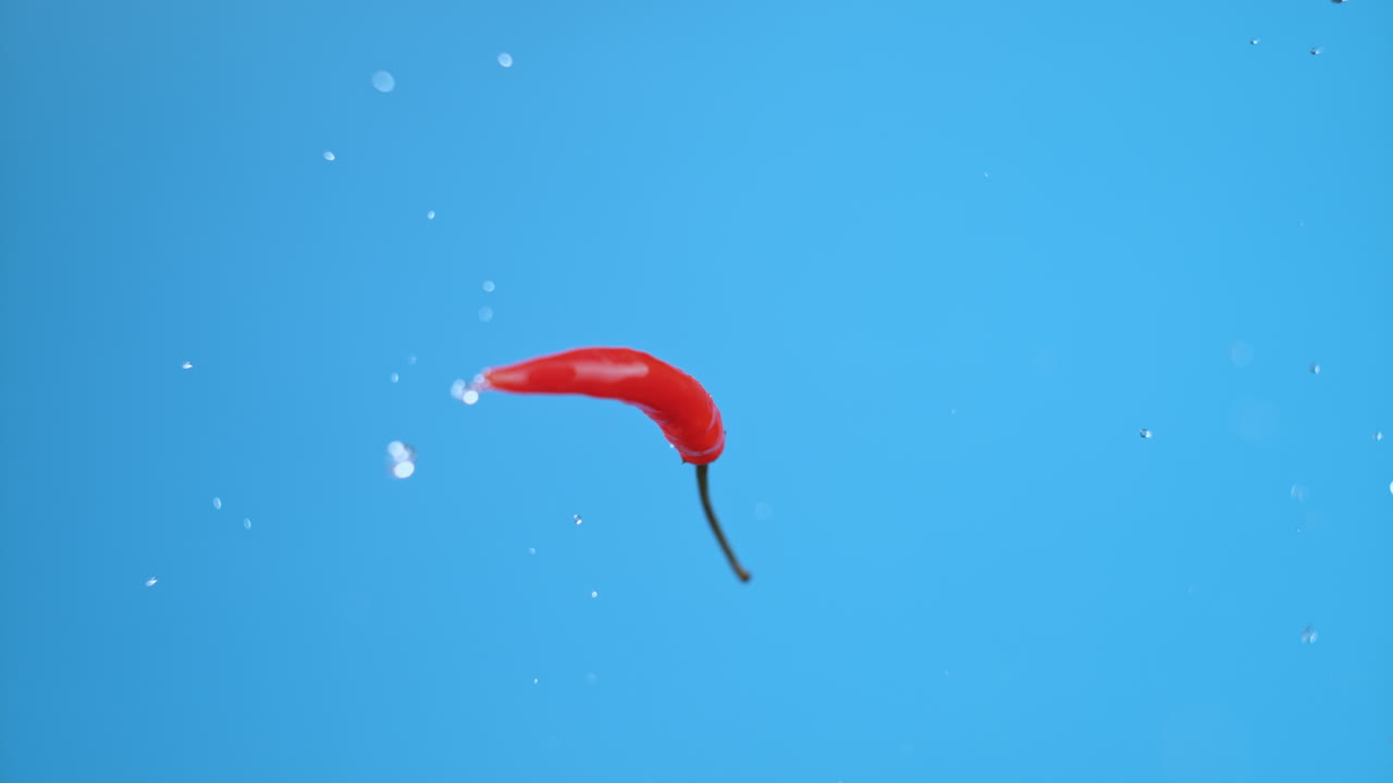 красный горячий чили летит вверх, дико вращается, брызгает водой.