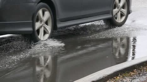 Close-up-of-car-tires-driving-through-standing-water-in-the-road-splashing-in-a-puddle,-Slow-motion