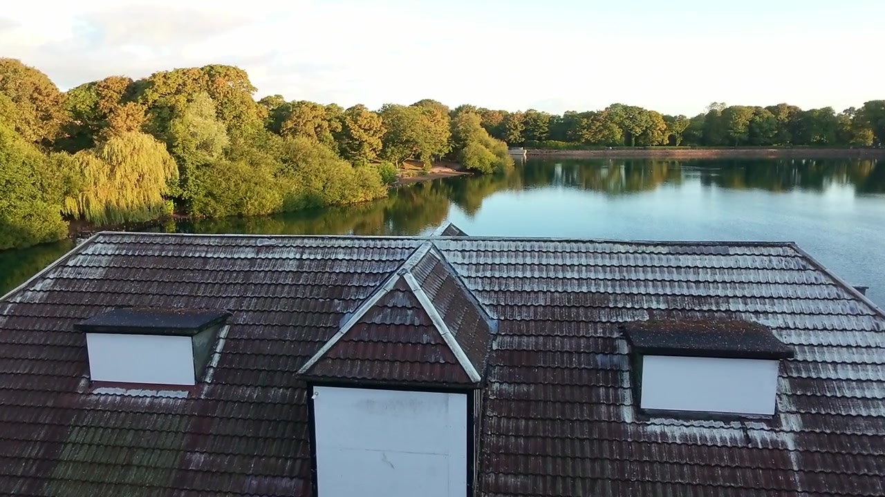Luftaufnahme eines verlassenen viktorianischen Park-Bootshauses über das Dach, die einen Waldsee bei Sonnenaufgang enthüllt