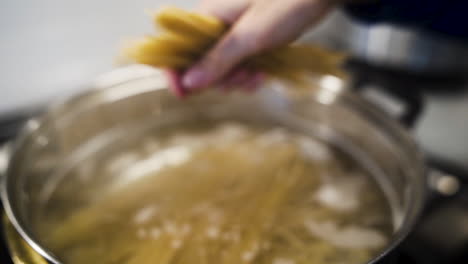 cook breaking spaghetti noodles and dropping them into a pot in slow motion