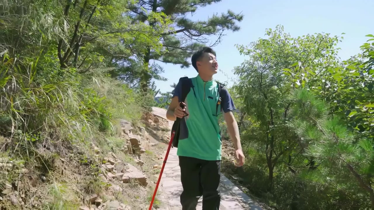 Un escursionista stanco con uno stile di vita attivo, con zaino in spalla e bastoncini, che si asciuga il sudore mentre fa trekking o jogging lungo un sentiero di montagna e un percorso forestale attraverso un paesaggio alpino, incarnando il concetto di avventura e libertà all'aria aperta.