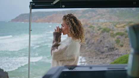 morning lady drinking coffee looking on amazing ocean waves. curly woman tourist