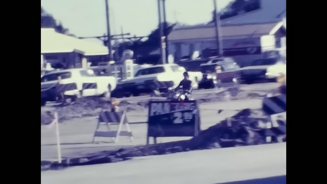 Man Riding Motorcycle Down Street in 1970s USA. CIRCA USA - 1970s: A man cruises down a street on a motorcycle in 1970s USA.