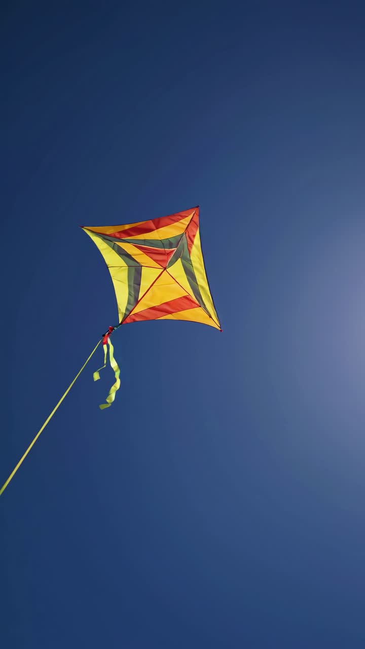 A vibrant kite soaring in a clear blue sky, captured from a low-angle, evokes freedom and joy