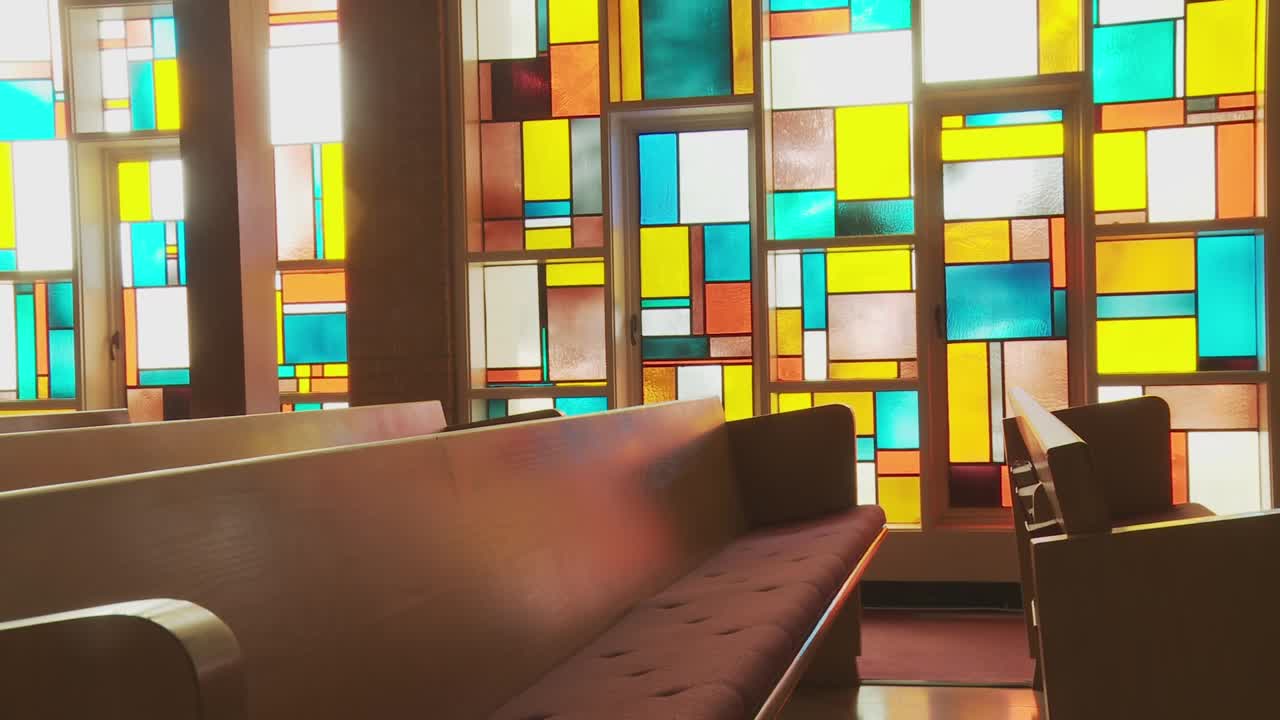 empuje la plataforma rodante en un banco vacío de la iglesia enmarcado por una impresionante pared de vidrieras que florece con colores vibrantes