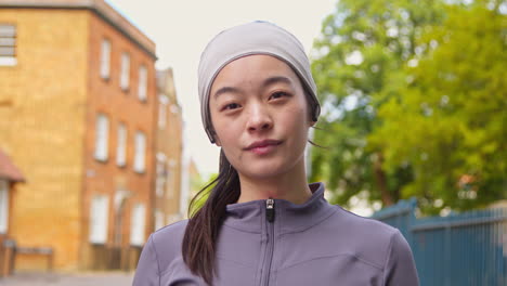 close up portrait of young woman exercising about to run along urban street wearing wireless earbuds 1