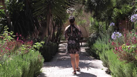 Girl-strolling-through-a-lush-garden-park,-surrounded-by-vibrant-flowers-and-greenery