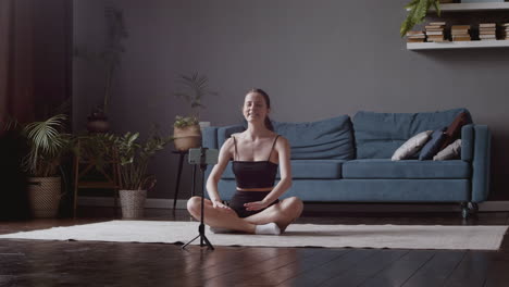 young attractive girl giving an online yoga lesson through the smartphone camera and practices the breaths