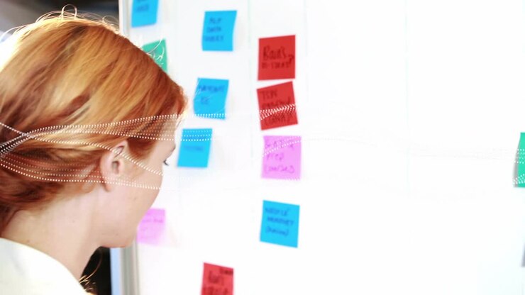 Project lead woman spotting red note on white board and moving sticky notes for sprint planning
