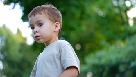 little boy picks a small ball from the grass. toddler tosses the ball and watches it fall. baby playing outdoors in summer.